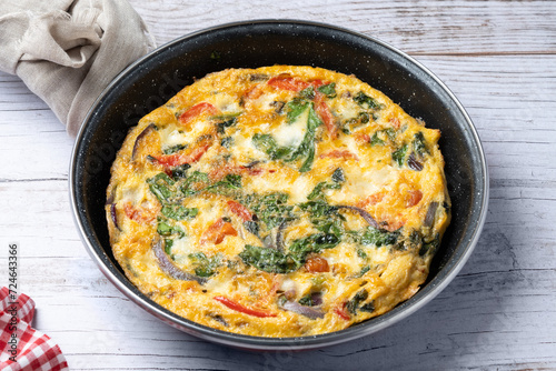 Italian Frittata made with spinach, tomatoes, onion and peppers on white wooden table