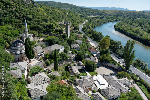 Medieval town Pocitelj with mosque and clock tower on bank of Neretva river during sunny day photo