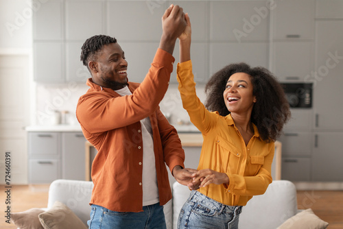 Cheerful millennial black spouses having fun together dancing in kitchen