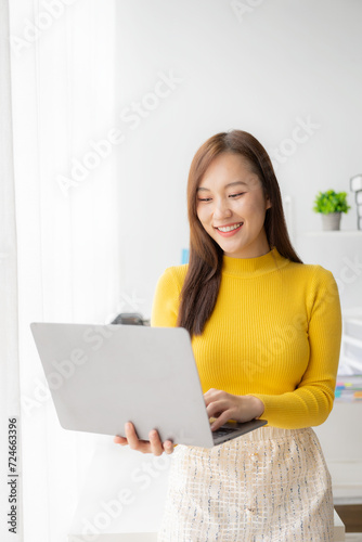Young Asian woman sits at a table and calculates financial graphs showing investment results. Plan your business growth process with financial review and budgeting using a calculator and laptop. © MrAshi