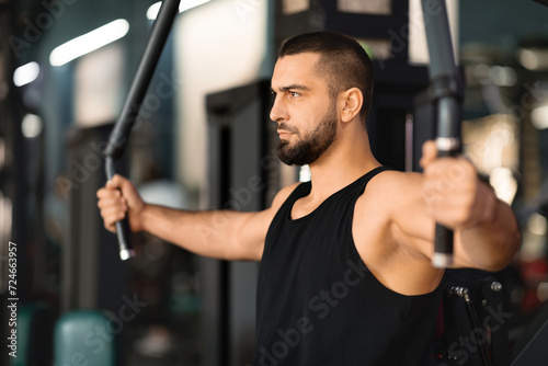 Concentrated man in tank top exercising on chest press machine at gym