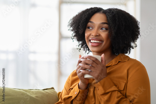 Glad pensive millennial black lady enjoy cup of coffee in hands, free time photo