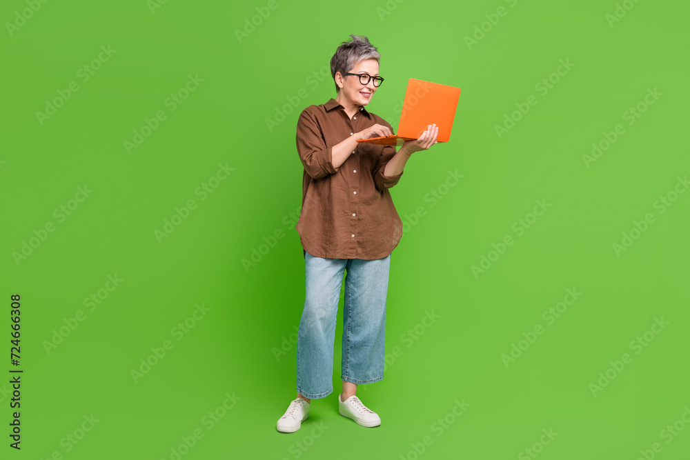 Full size photo of intelligent cheerful person wear stylish shirt look at laptop write post in blog isolated on green color background Full size photo of intelligent cheerful person wear stylish shirt look at laptop write post in blog isolated on green color background