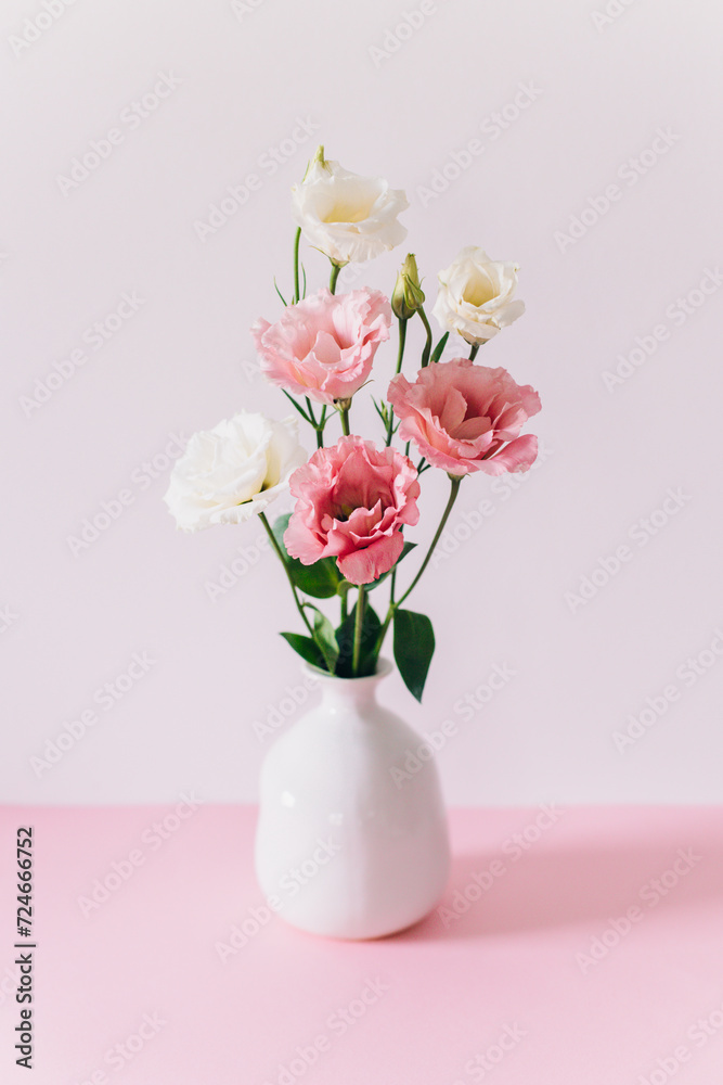 Beautiful white and pink Eustoma (Lisianthus) flowers in a vase on a pink pastel background.