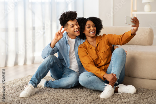 A radiant young couple in casual attire shares a playful moment, taking a cozy selfie