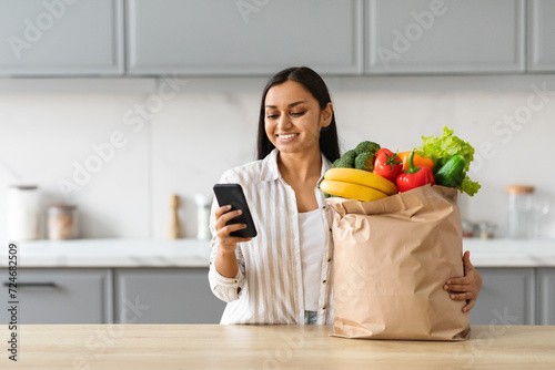 Cheerful young indian woman order grocery online photo