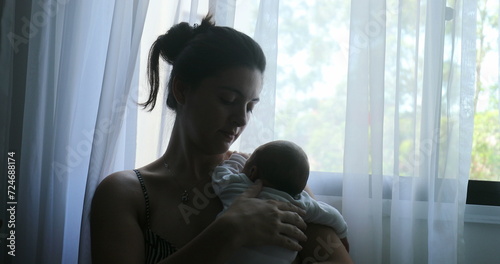 Mother holding newborn baby next to window