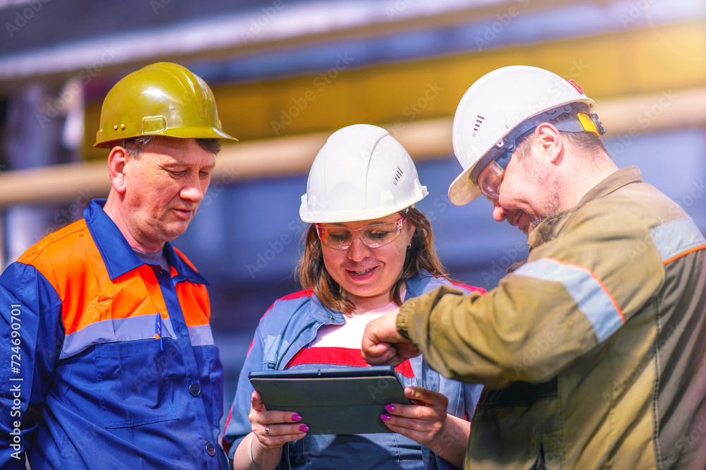 A professional team of male and female engineers are discussing a new project using a tablet.Workers are talking about plans. They work at a metal structures factory.Sun glare. A professional team of male and female engineers are discussing a new project using a tablet.Workers are talking about plans. They work at a metal structures factory.Sun glare.
