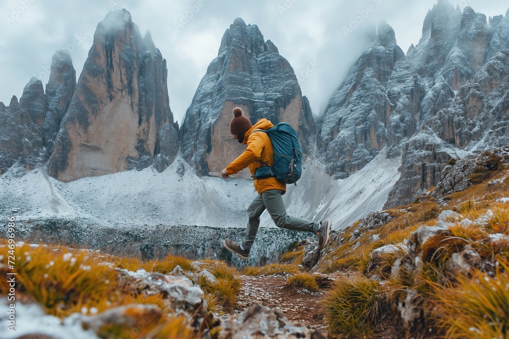 An adventurous hiker jumps between the rocks, with a backpack and raincoat, among the high alpine mountains.