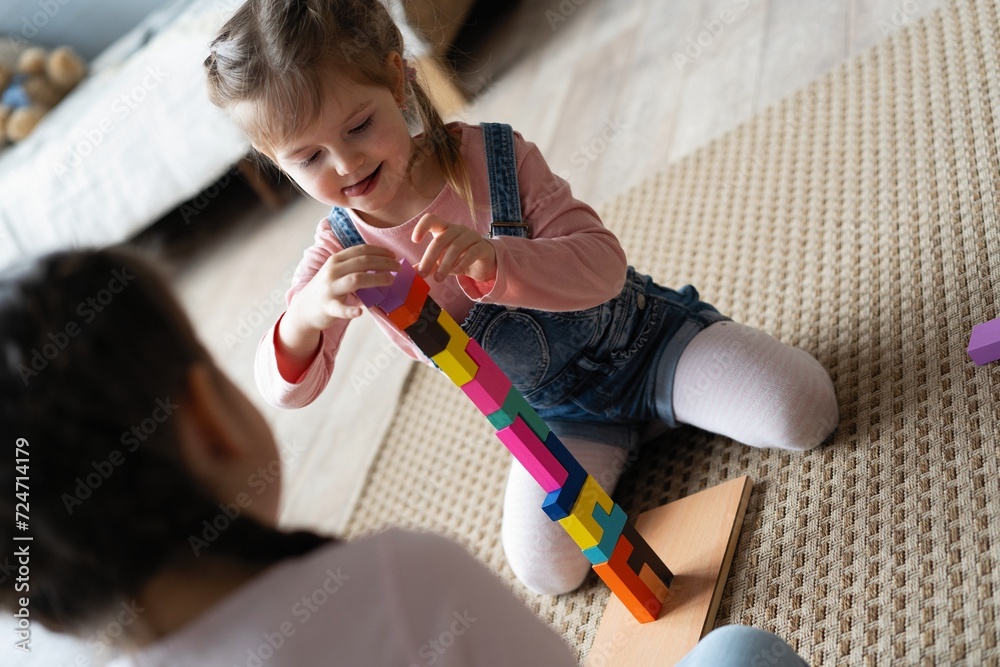 Two little 6s 7s sisters pretty daughters spend free playtime seated on carpet warm floor in modern living room play together wooden brick toys set