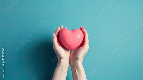 Hands tenderly clasping a red heart against a serene blue background. photo