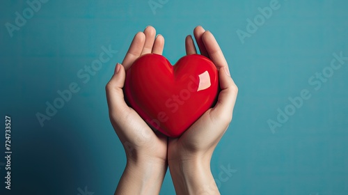 Hands tenderly clasping a red heart against a serene blue background.