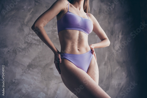 Photo of gorgeous woman posing in trendy purple lingerie touch waist isolated on grey concrete wall background © deagreez