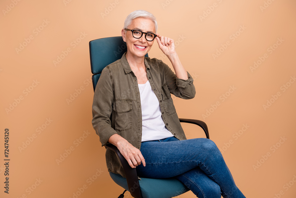 Photo portrait of attractive retired woman sit armchair confident manager dressed stylish khaki clothes isolated on beige color background Photo portrait of attractive retired woman sit armchair confident manager dressed stylish khaki clothes isolated on beige color background