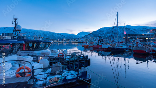 Twilight view of Tromsø port with snow-covered mountains and bridge in Norway.