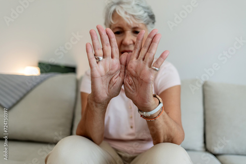 Photo of Painful Wrist In An Elderly Person. Senior woman suffering from pain in wrist at home while sitting on a gray sofa. Mature woman feeling wrist pain, injury problem, healthcare concept, sprain photo