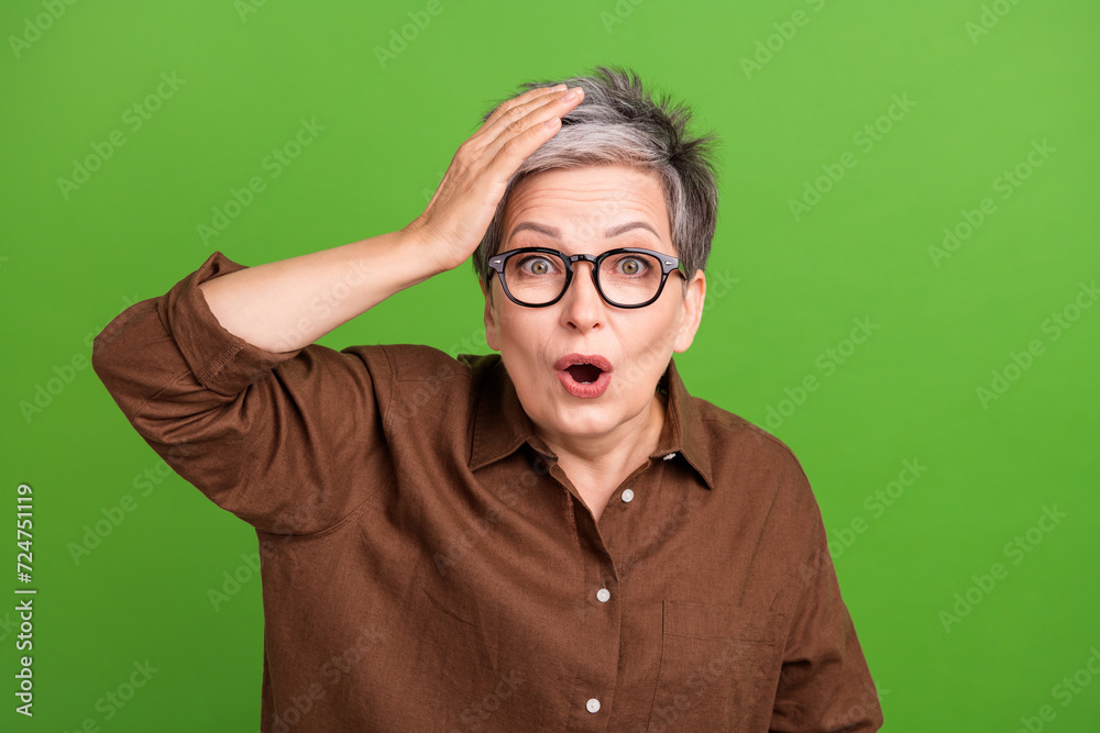 Photo of astonished woman with short hair wear brown shirt palm on head staring at sale open mouth isolated on green color background Photo of astonished woman with short hair wear brown shirt palm on head staring at sale open mouth isolated on green color background