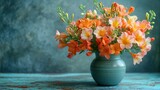  a vase filled with orange and pink flowers on top of a blue and green tablecloth covered table next to a gray and green wall with a blue wall in the background.