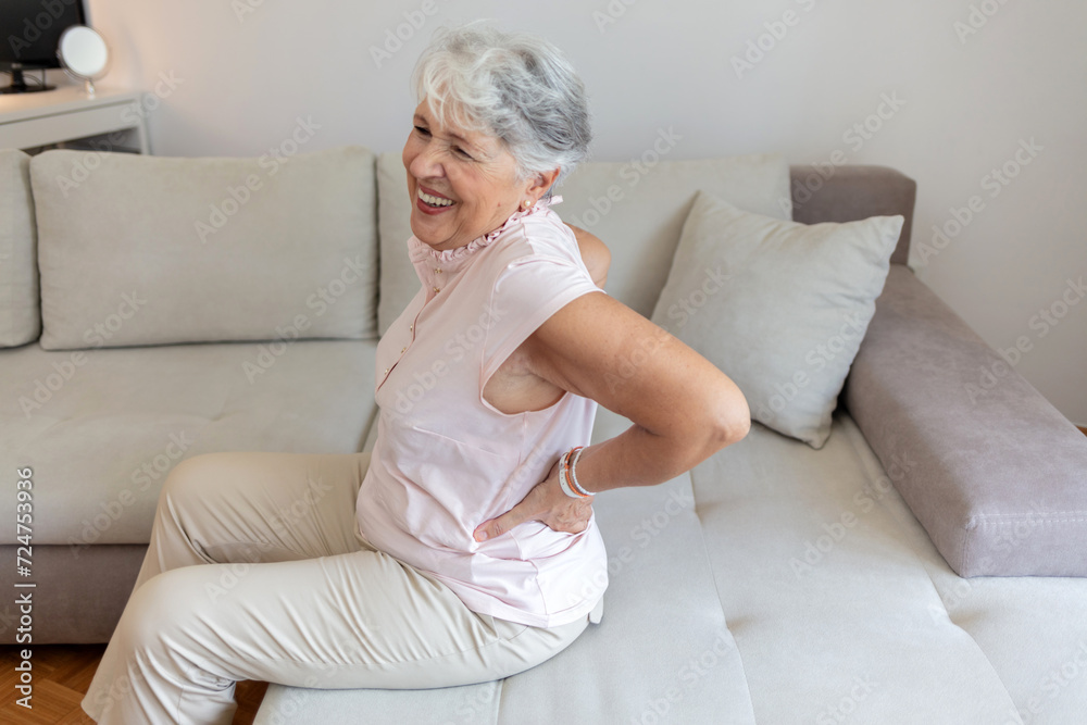 A senior Caucasian woman struggling with bad backache alone at home. Old woman having back pain in the livingroom at home. Elderly woman suffering from backache at home. A senior Caucasian woman struggling with bad backache alone at home. Old woman having back pain in the livingroom at home. Elderly woman suffering from backache at home.