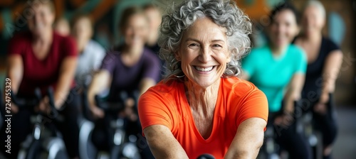 Active senior woman with grey hair exercising on exercise bike with group of people in gym