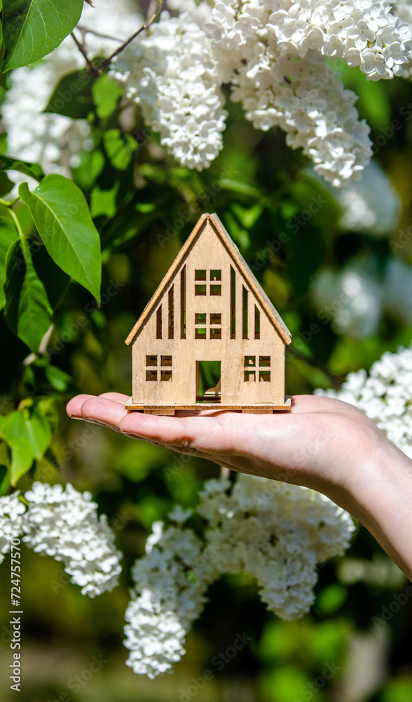 Φωτογραφία The girl holds the house symbol against the background of blossoming white lilac