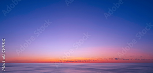 Fototapeta Naklejka Na Ścianę i Meble -  Idyllic natural sunrise sky background over sea in the early morning with motion blur of flowing water surface in panoramic view, beautiful tranquil seascape view in sunset time 