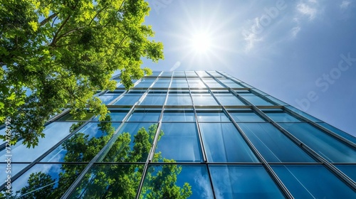 Sunlight filters through green leaves onto a modern glass building, mirroring nature