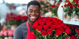 Cute smiling African American male flower seller in a flower shop, wearing an apron with a large bouquet of red roses. Gardening, floristry and holidays concept