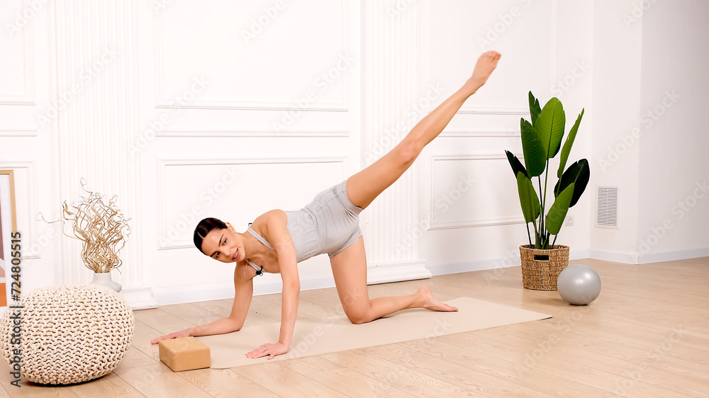A beautiful young woman with collected hair, dressed in a stylish sports uniform, conducts a workout in the studio against a light background. Advertising for health, athletic body, yoga clothes. A beautiful young woman with collected hair, dressed in a stylish sports uniform, conducts a workout in the studio against a light background. Advertising for health, athletic body, yoga clothes.