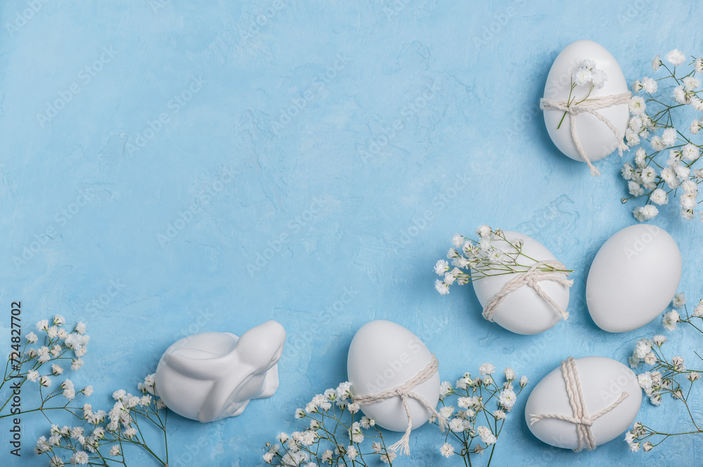 Obraz premium White Easter eggs decorated with twine and sprigs of gypsophila on a blue background. Easter greeting concept.Easter background.