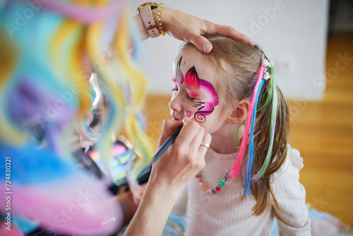 Artist painting little preschooler girl like unicorn on a birthday party. Creative activities for kids photo