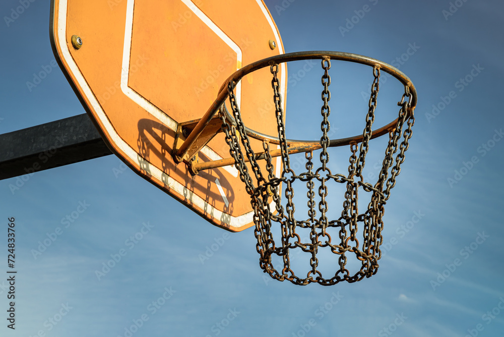 Side view of Basketball backboard with the hoop metal ring and steel chain net against blue sky background seen from below. Street basketball court, Low angle view, Look up, Copy space,Selective focus