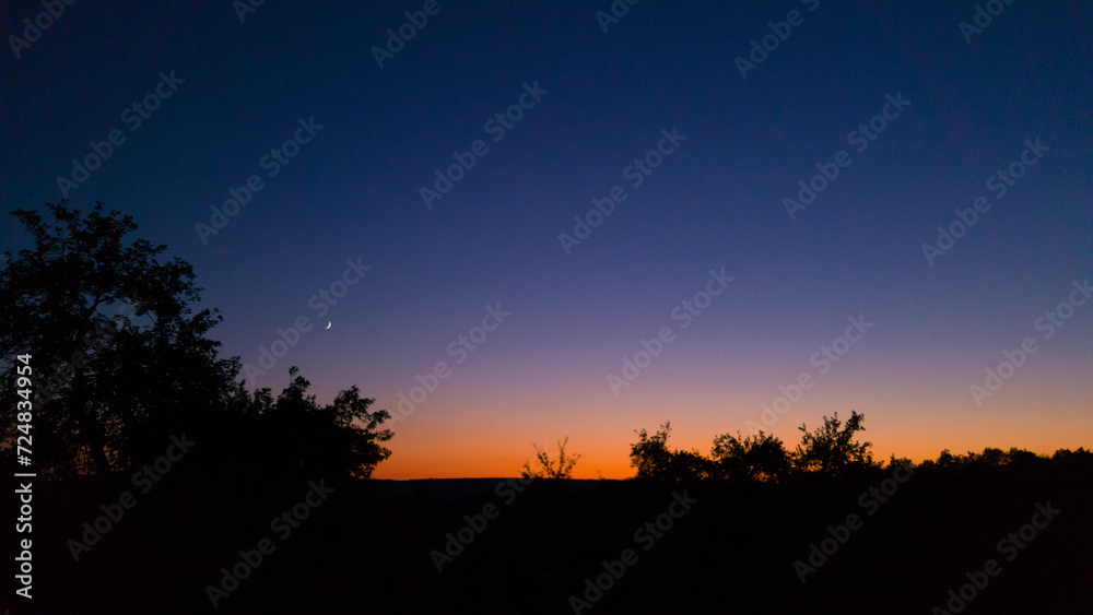 Young crescent moon on a clear sky at the end of the day in the summer