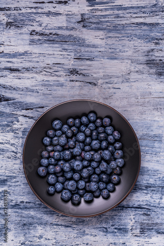 from above, on a textured background, a black plate with fresh blueberries. Empty space.