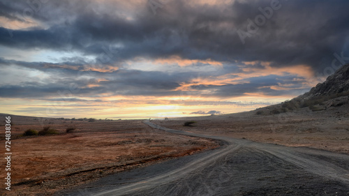 The road with a car in a distance in Boa Vista island desert  landscape leads to horizon under a dramatic sunset sky. Cape Verde.