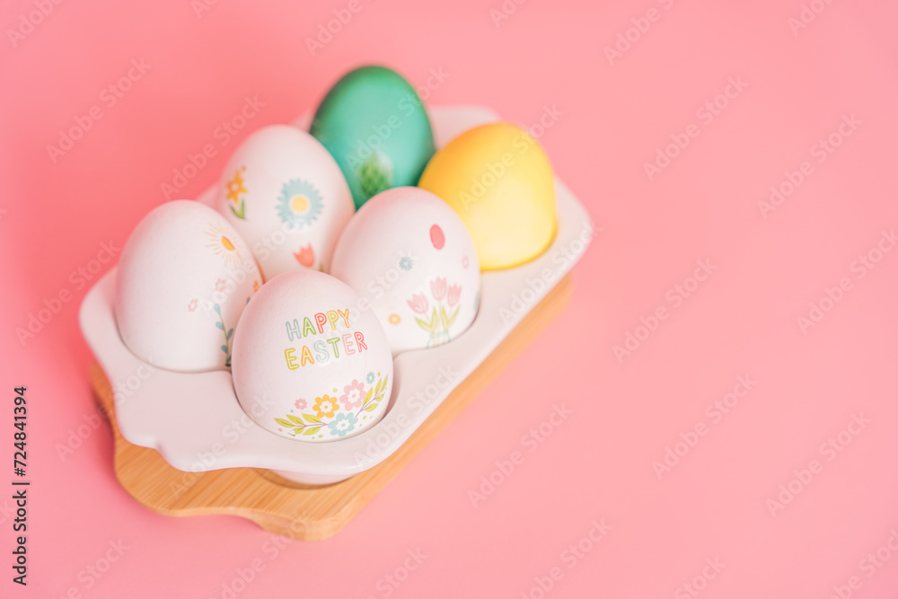 Easter eggs of different colors and in stickers in a white tray on a pink background.
