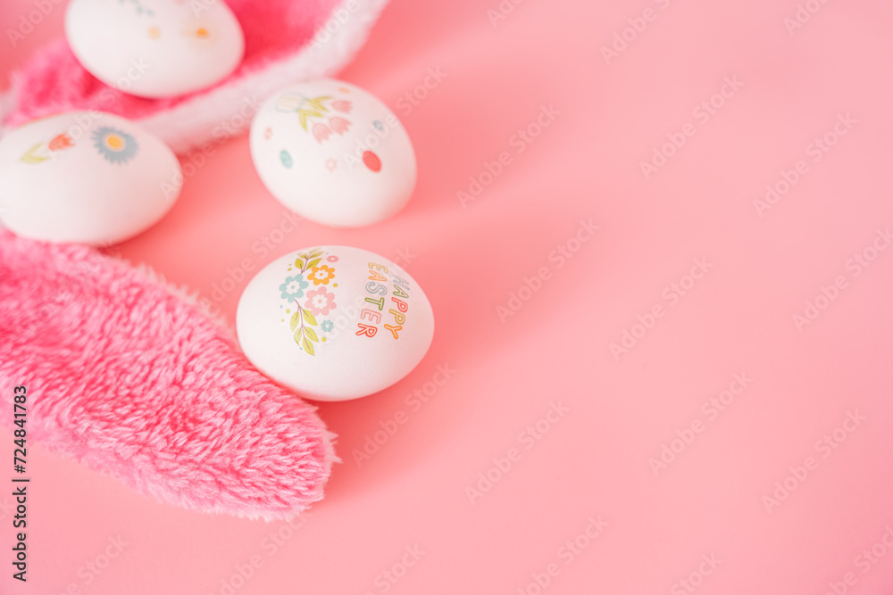 Easter eggs with drawings and stickers and bunny ears on pink background.