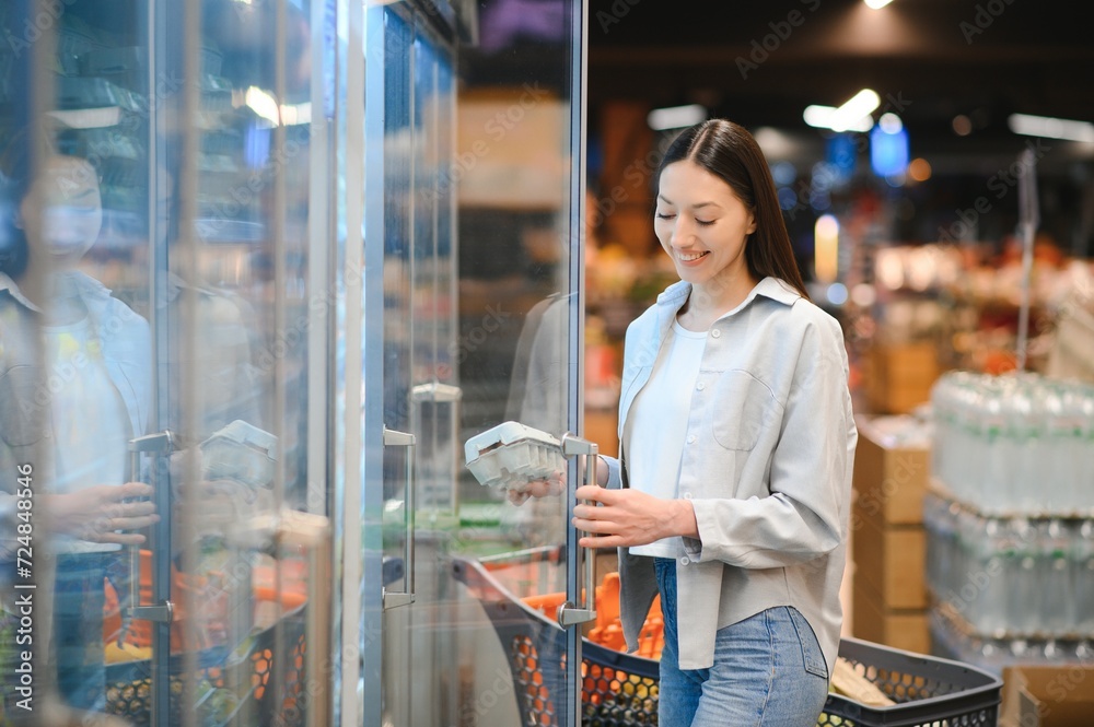 Young smiling happy woman 20s in casual clothes shopping at supermaket store with grocery cart