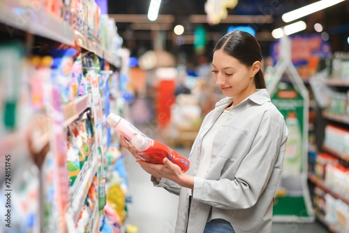 Interested young woman making purchases in household chemicals store, reading labels on bottles