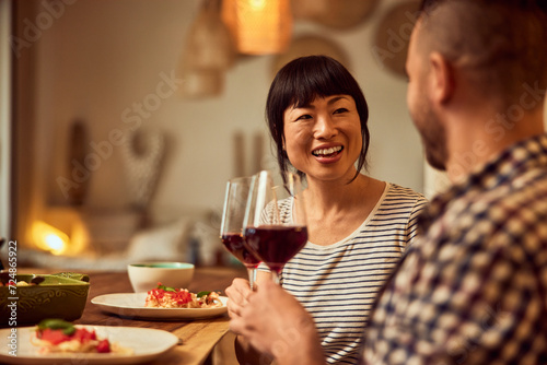 A smiling lovely couple having dinner at home, drinking wine, focus on the Asian female.