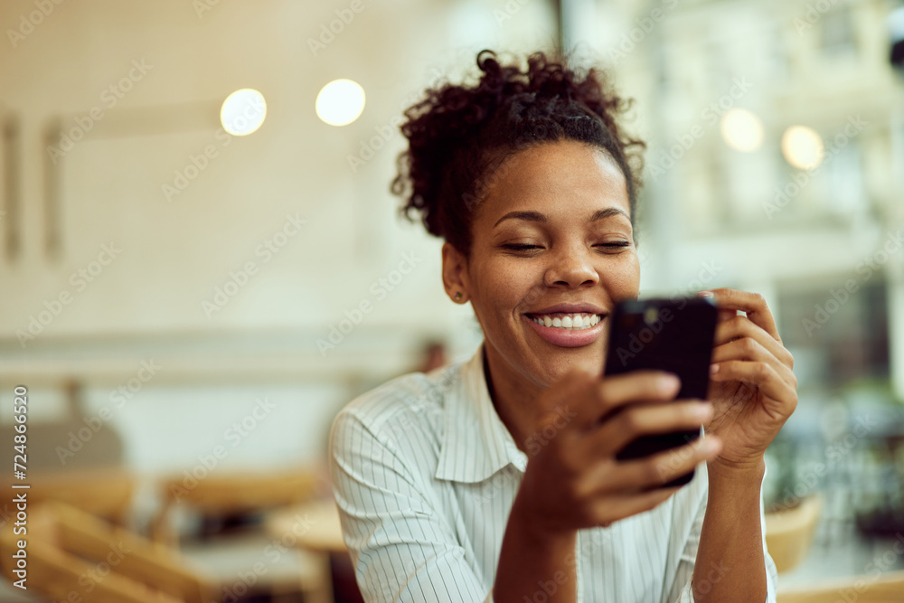 A smiling African woman sitting at the cafe, using a mobile phone. A smiling African woman sitting at the cafe, using a mobile phone.