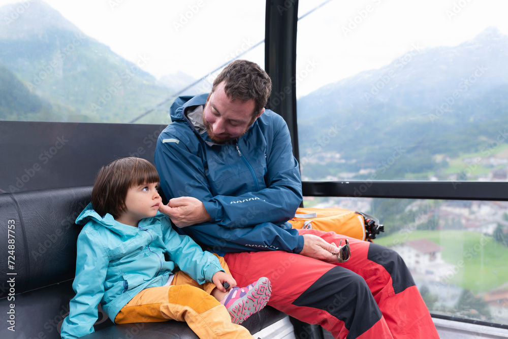 Father caressing his little daughter while they are moving up in a cable car of a ski resort during summer season. Father caressing his little daughter while they are moving up in a cable car of a ski resort during summer season.