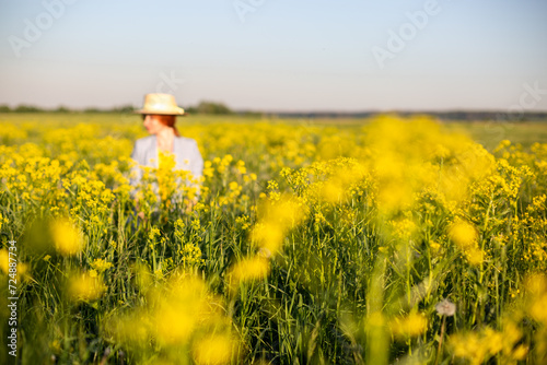 girl in an out-of-focus hat on a blooming yellow rapeseed field.