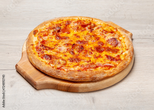 Meat pizza with ham, sausage and cheese on a wooden board