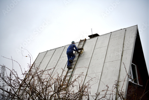 The roof roofer climbs up the ladder to the roof of the house to fix sheet metal roof photo