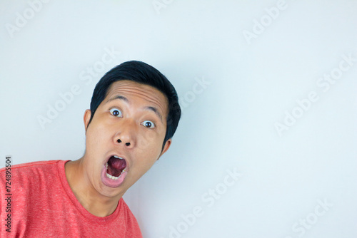 funny expression of shocked and surprised Asian man wearing a red t-shirt looking at the camera photo
