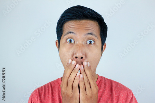 funny expression of shocked and surprised Asian man wearing a red t-shirt looking at the camera photo