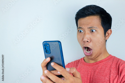 funny facial expression of asian man shocked and shocked holding and looking at phone screen photo