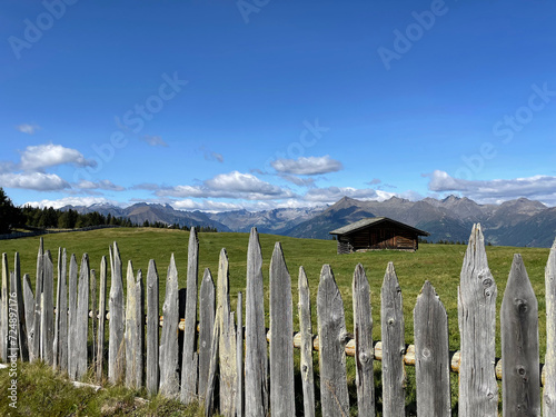 typical wooden fence of Rodenecker alm in northern Italy with a wooden cabin and the Dolomiti mountains in the distance