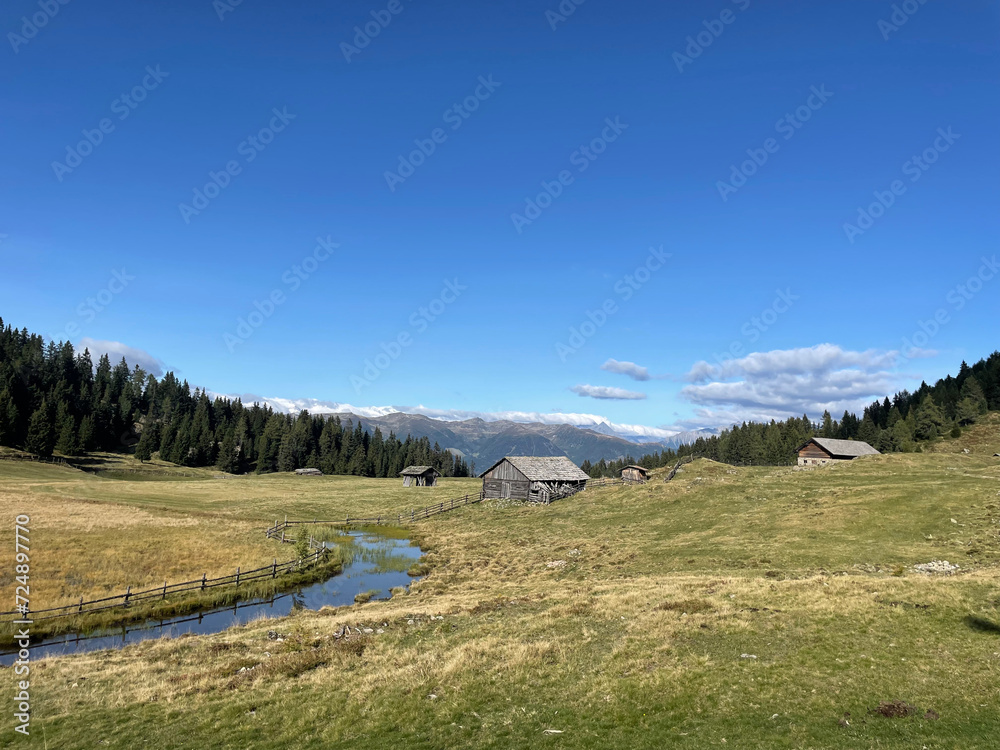 pastoral landscape with wooden mountain cabins spread over an open mountain meadow with a small creek